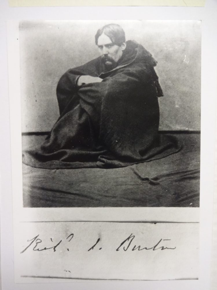 Sir Richard Burton sitting on the floor wearing jubbah with signature