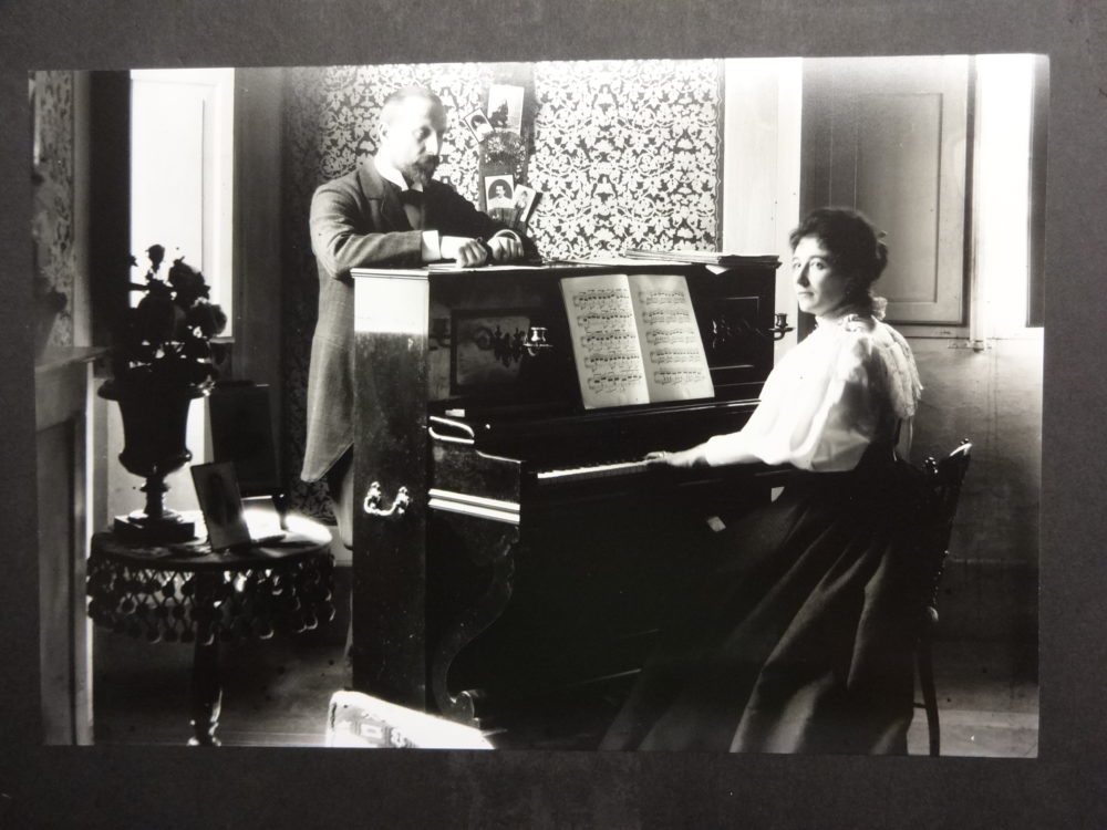 Dr Baker standing behind a piano with his sister/wife playing