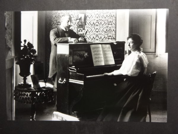 Dr Baker standing behind a piano with his sister/wife playing