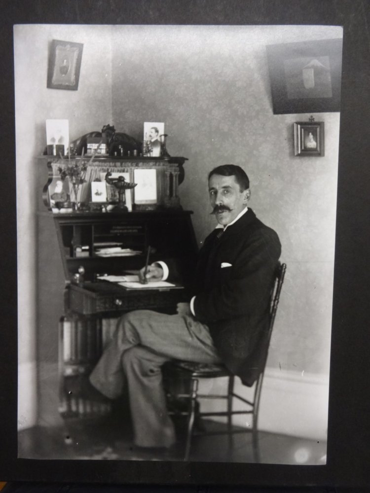 A black and white photograph of a man sitting crossed legged at a desk.
