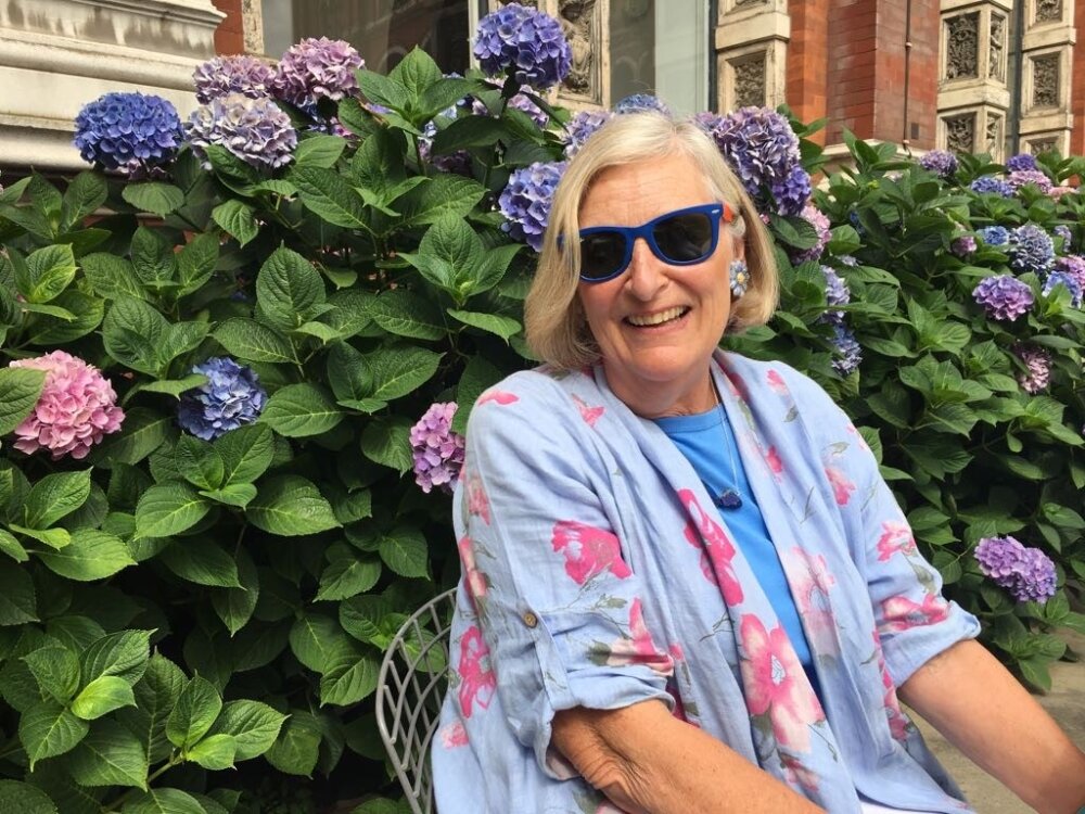 Portrait of Jill Storey, seated in front of purple flowers