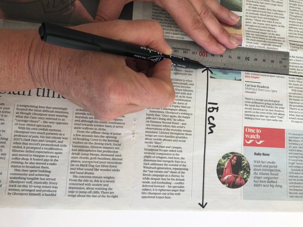 A hand drawing a 15cm line onto newspaper with a ruler.